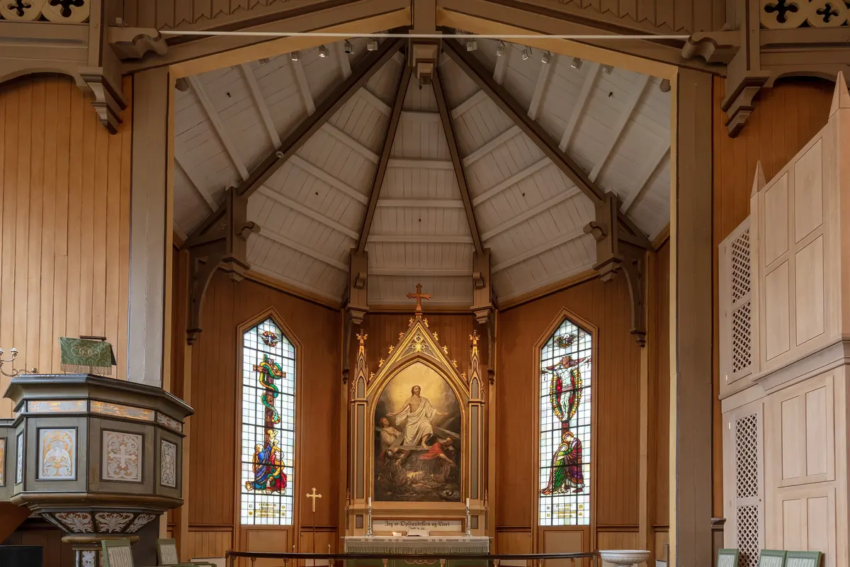 The altar of Tromsø Cathedral with a gilt frame around a painting of the Resurrection, a pulpit on the left and two tall stained-glass windows