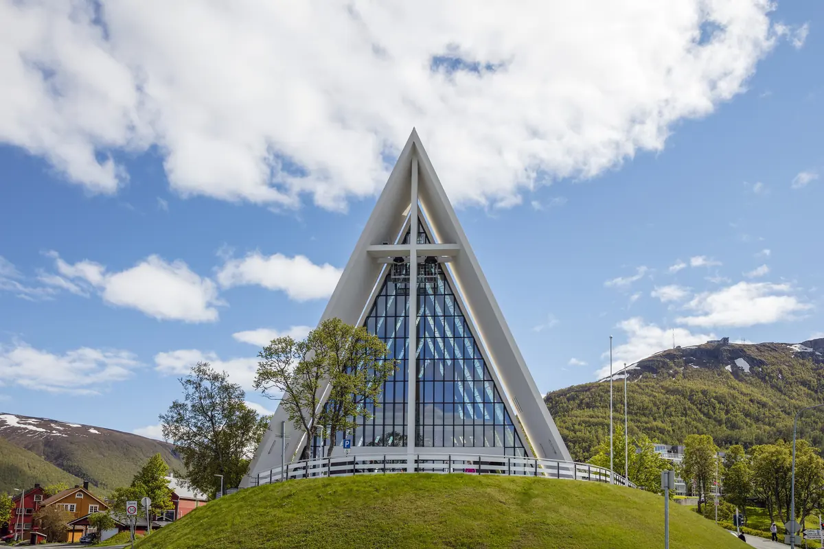 The white, triangular glass front of the Arctic Cathedral in Tromsdalen under a blue sky, a separate church from the concert venue