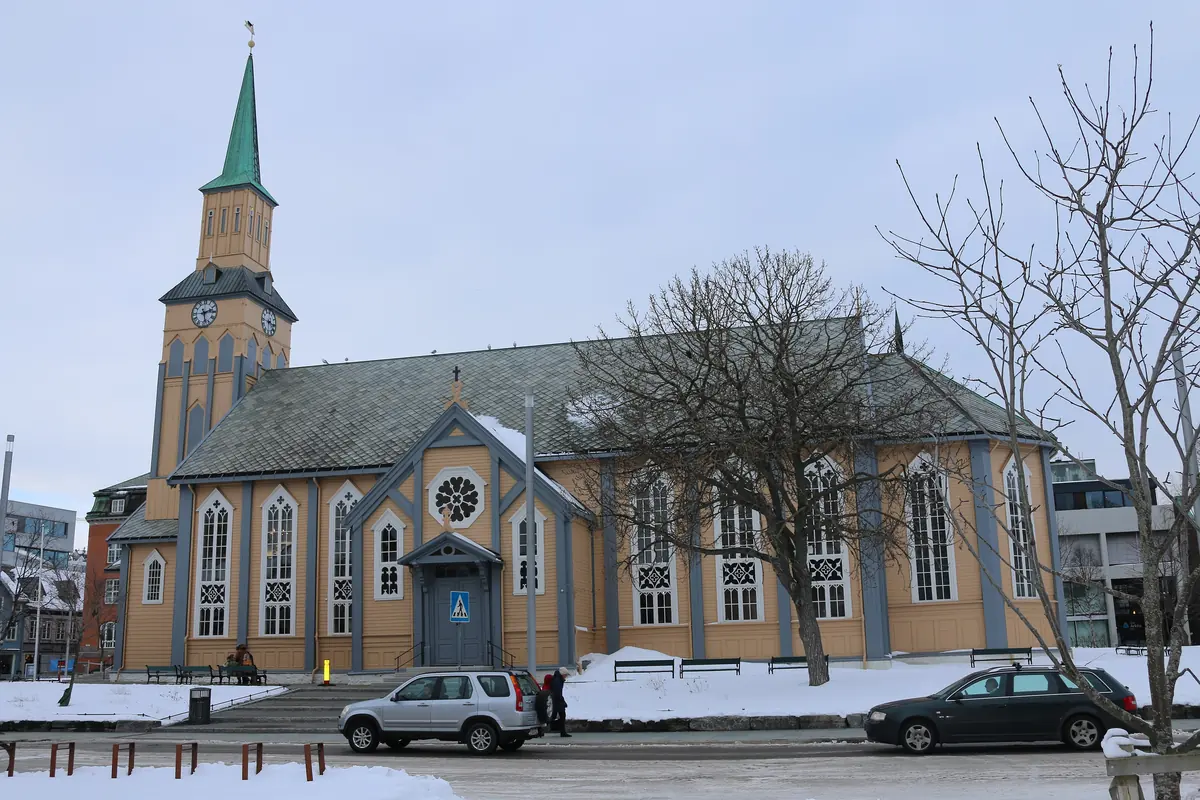 The yellow wooden Tromsø Cathedral with its pointed tower, seen from the side across a snowy street
